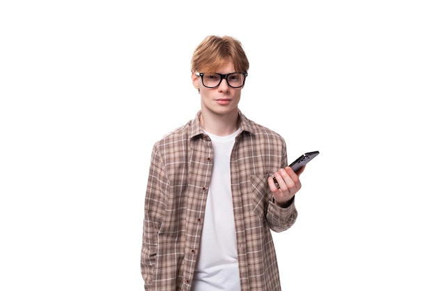 Jovem caucasiano com cabelo ruivo e camisa usa ativamente um smartphone