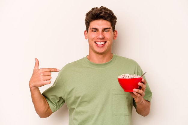 Jovem caucasiano comendo cereais isolados em fundo branco pessoa apontando com a mão para um espaço de cópia de camisa orgulhoso e confiante