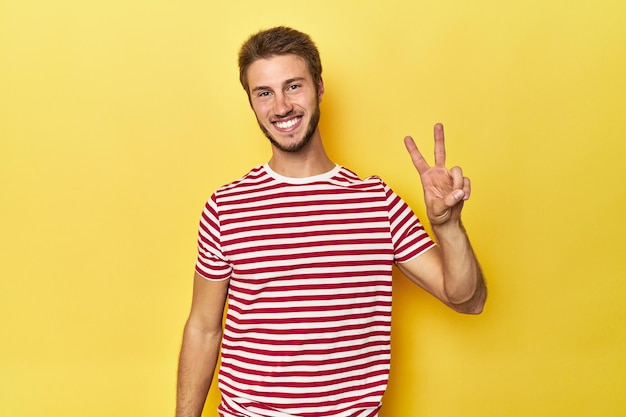 Jovem caucasiano em um fundo de estúdio amarelo, alegre e despreocupado, mostrando um símbolo de paz