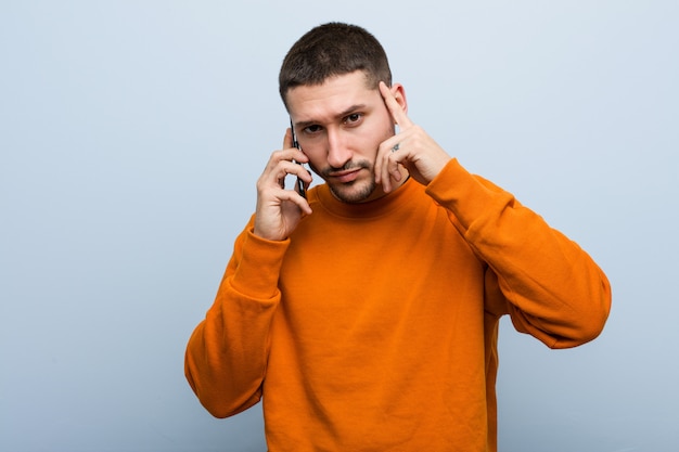 Jovem, caucasiano, homem, segurando, um, telefone, apontar, seu, templo, com, dedo, pensando