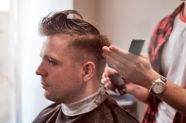 Jovem caucasiano na barbearia Barber está cortando o cabelo no estilo hipster