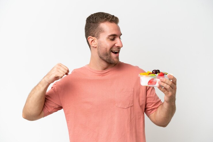 Foto jovem caucasiano segurando uma tigela de frutas isolado em fundo branco celebrando uma vitória