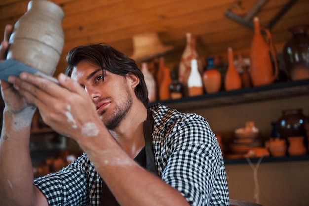 Jovem ceramista segura a panela artesanal fresca na mão e analisa os resultados de seu trabalho.