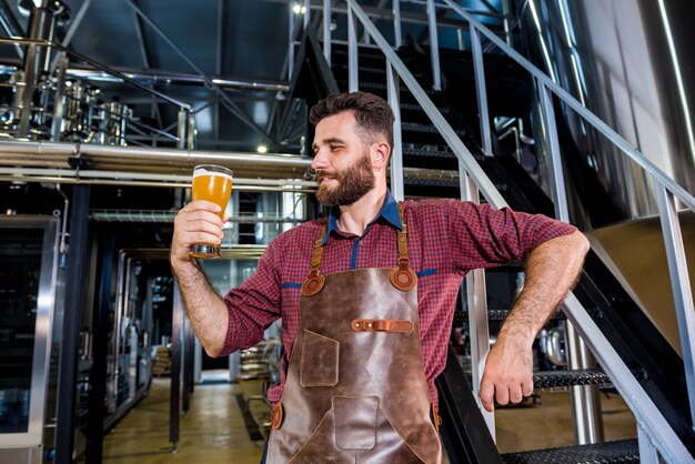 Jovem cervejeiro com avental de couro em uma moderna fábrica de cerveja