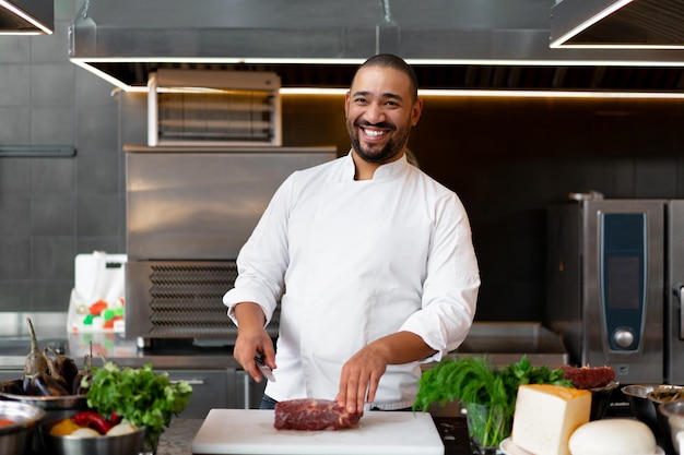 Jovem chef africano bonito de pé na cozinha profissional em um restaurante preparando uma refeição de carne