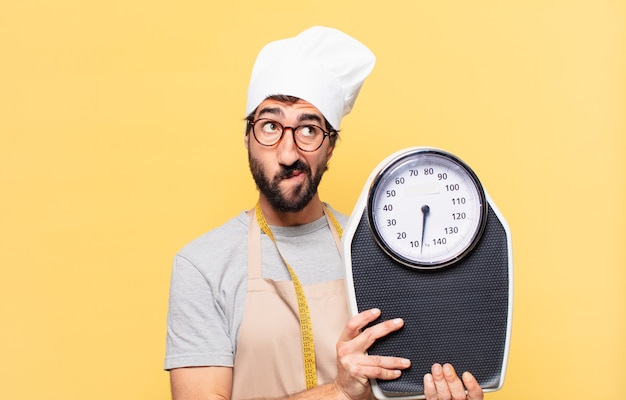 Jovem chef barbudo duvidando ou com uma expressão incerta e segurando uma balança