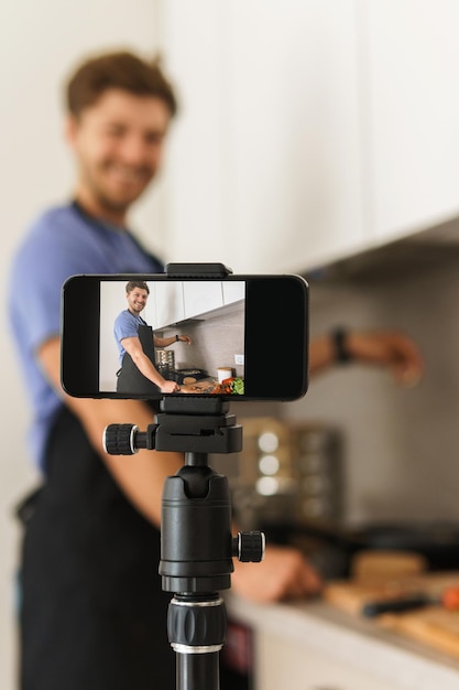 Foto jovem chef barbudo está cozinhando na cozinha e sorrindo para a câmera