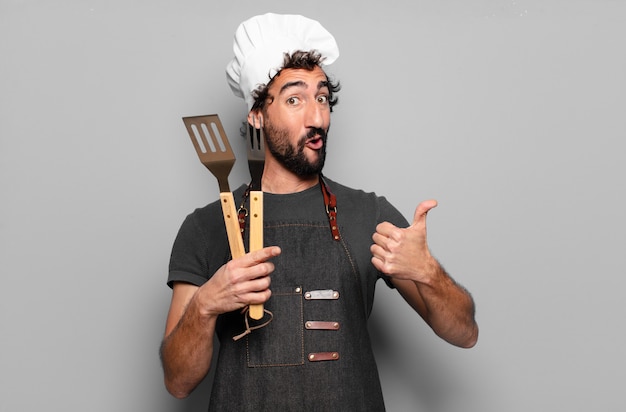 Jovem chef barbudo segurando utensílios de cozinha