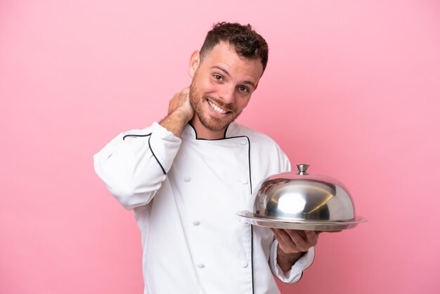 Jovem chef brasileiro com bandeja isolada no fundo rosa rindo