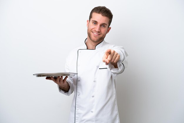Jovem chef caucasiano com bandeja isolada no fundo branco, apontando para a frente com expressão feliz