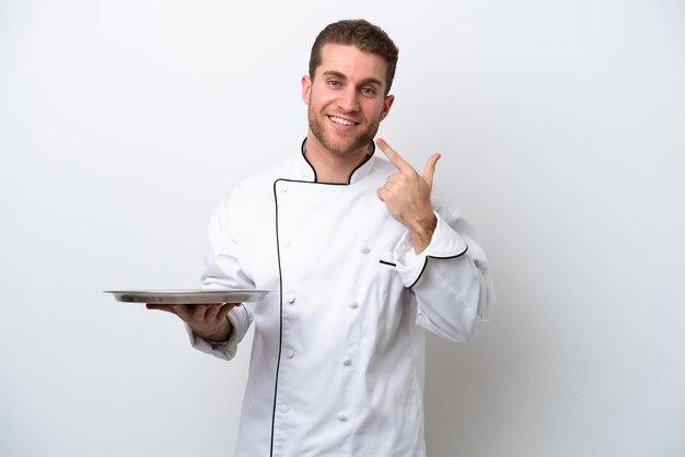 Jovem chef caucasiano com bandeja isolada no fundo branco, dando um polegar para cima gesto
