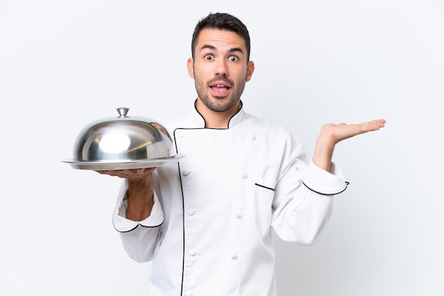 Jovem chef com bandeja isolada no fundo branco com expressão facial chocada