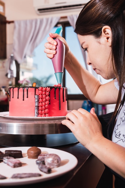 Jovem chef confeiteira profissional a decorar um bolo colorido.