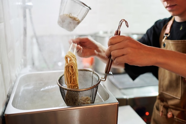 Jovem chef de avental colocando ramen cozido quente em uma peneira sobre uma pia metálica