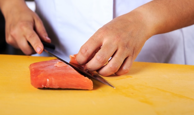 Jovem chef feminino coock vestido com uniforme branco corta peixe salmão em cima da mesa na cozinha do restaurante