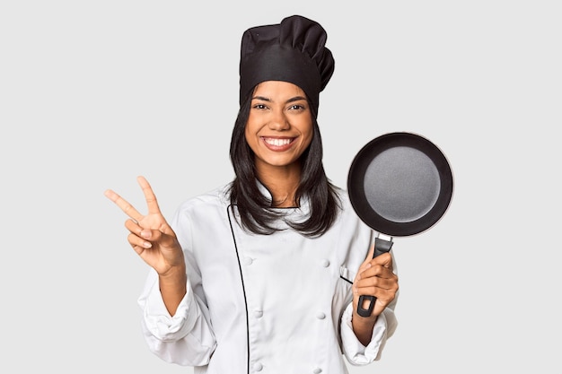 Jovem chef filipino segurando a panela pelo punho mostrando o número dois com os dedos