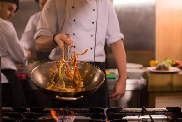 Jovem chef masculino lançando legumes no wok na cozinha comercial