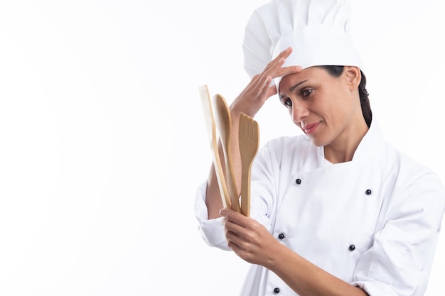 Jovem chef preocupado caucasiano com roupa de chef enquanto segura utensílios de cozinha isolados no fundo branco com espaço de cópia