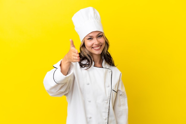 Jovem chef russa isolada em fundo amarelo apertando as mãos para fechar um bom negócio