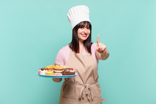 Jovem chef sorrindo com orgulho e confiança fazendo a pose número um triunfantemente, sentindo-se uma líder