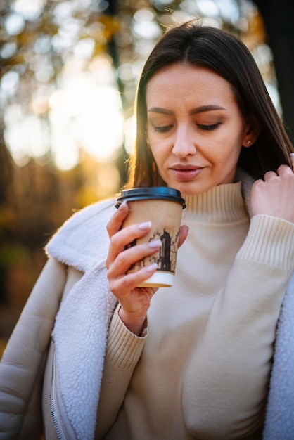 Jovem cheirando café no parque de outono Mulher ao ar livre desfrutando de café