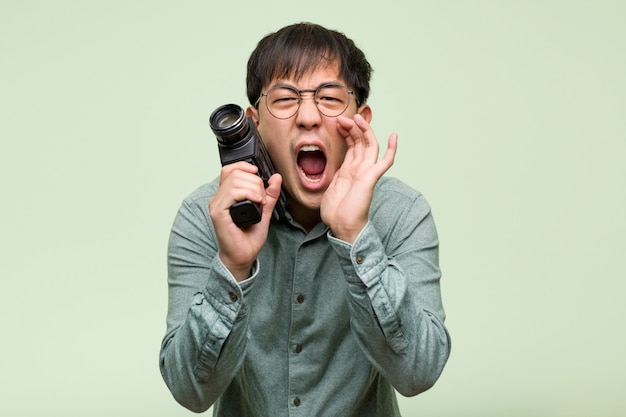 Jovem chinês segurando uma câmera vintage gritando algo feliz para a frente