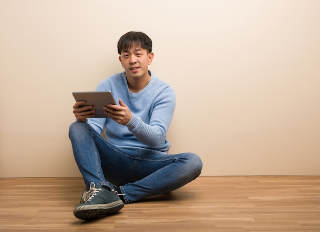 Jovem chinês sentado usando seu tablet alegre com um grande sorriso