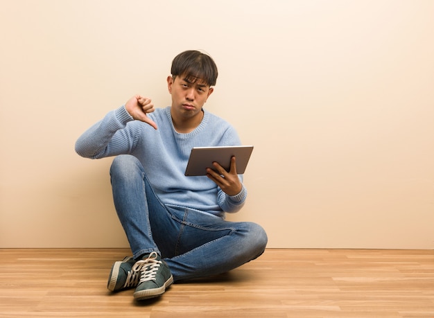 Jovem chinês sentado usando seu tablet, apontando os dedos, exemplo a seguir