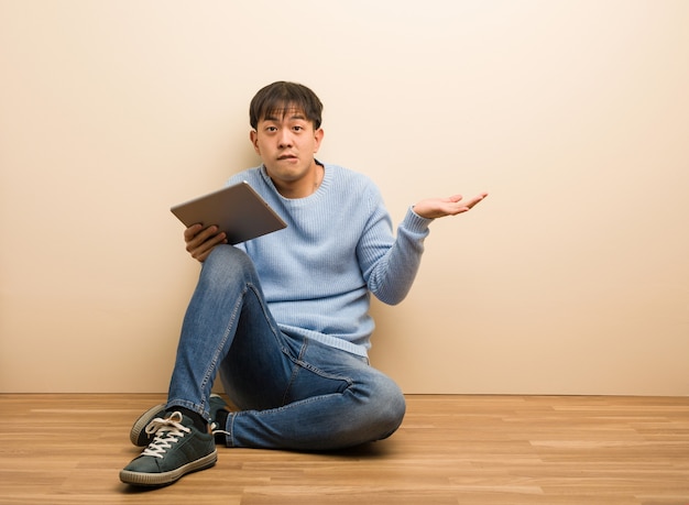 Jovem chinês sentado usando seu tablet confuso e duvidoso