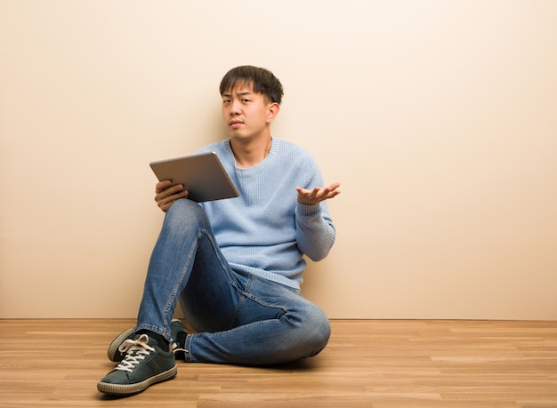 Jovem chinês sentado usando seu tablet confuso e duvidoso