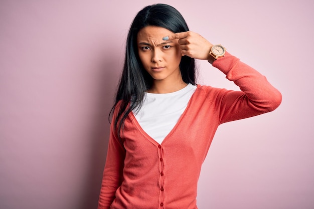 Jovem chinesa bonita vestindo suéter casual sobre fundo rosa isolado apontando infeliz para espinha na testa infecção feia de cravo Acne e problema de pele