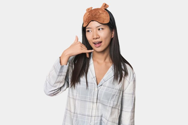 Jovem chinesa com máscara de pijama mostrando um gesto de chamada de telefone móvel com os dedos