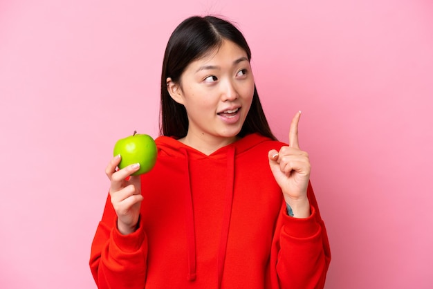 Jovem chinesa com uma maçã isolada em fundo rosa com a intenção de perceber a solução enquanto levanta um dedo