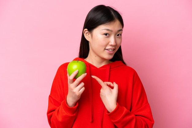 Jovem chinesa com uma maçã isolada em fundo rosa e apontando-a