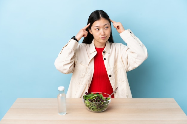 Jovem chinesa comendo uma salada com dúvidas e pensando