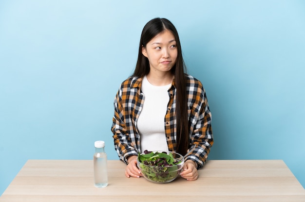 Jovem chinesa comendo uma salada com dúvidas enquanto olha para cima