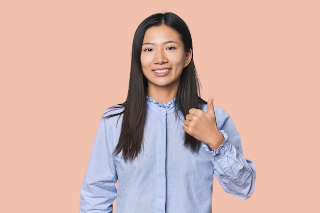 Jovem chinesa de camisa azul sorrindo e levantando o polegar