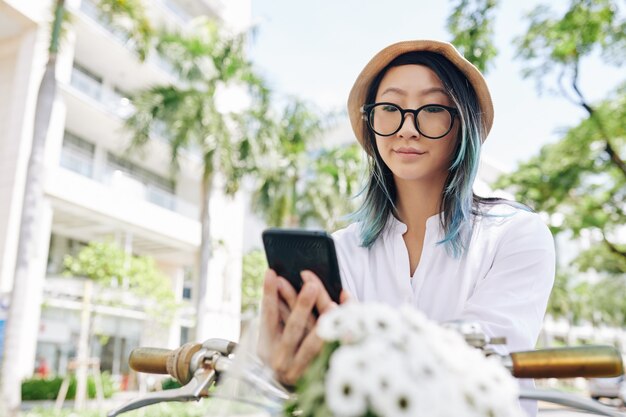 Jovem chinesa de óculos fazendo beicinho e pesquisando redes sociais via smartphone