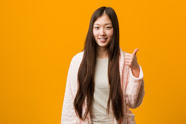 Jovem chinesa de pijama, sorrindo e levantando o polegar