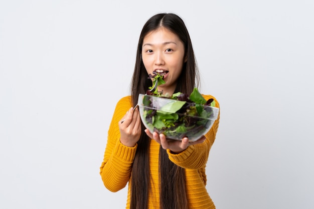 Jovem chinesa em branco isolado, segurando uma tigela de salada com expressão feliz
