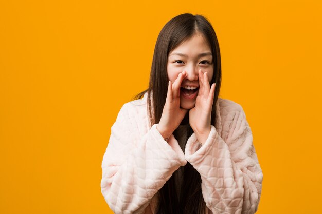 Jovem chinesa em pijama gritando animado para a frente.