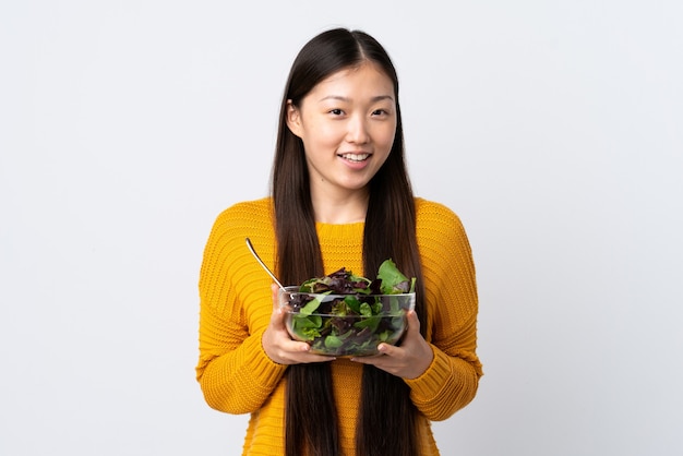 Jovem chinesa em um fundo branco isolado segurando uma tigela de salada com uma expressão feliz