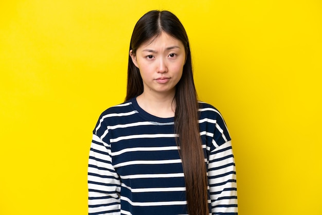 Jovem chinesa isolada em fundo amarelo com expressão triste