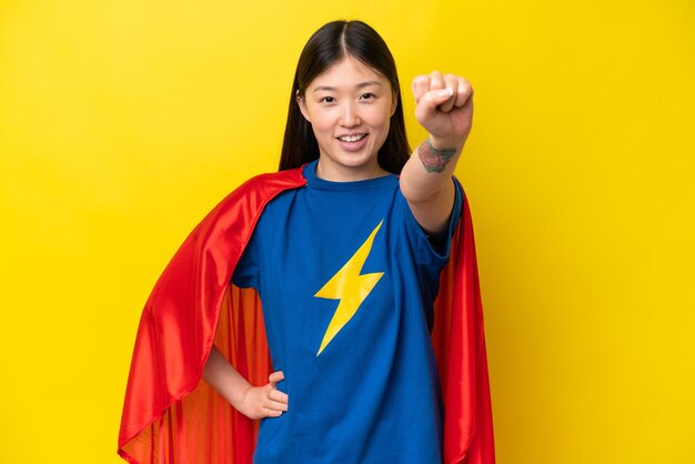 Jovem chinesa isolada em fundo amarelo em traje de super-herói com gesto orgulhoso