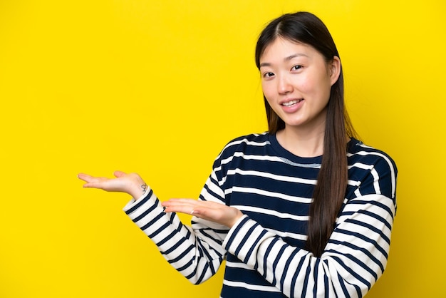 Jovem chinesa isolada em fundo amarelo, estendendo as mãos para o lado para convidar para vir