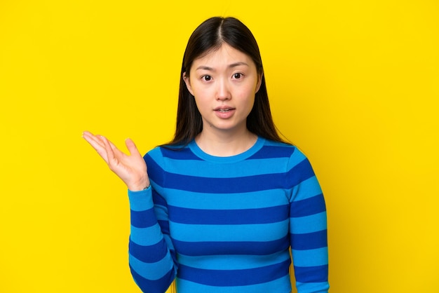 Jovem chinesa isolada em fundo amarelo fazendo gesto de dúvidas