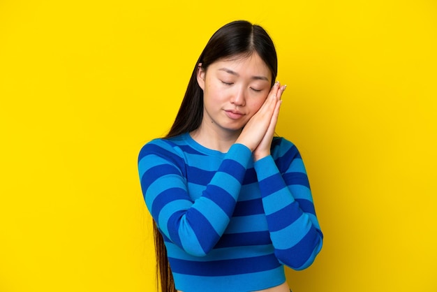 Jovem chinesa isolada em fundo amarelo fazendo gesto de sono em expressão adorável