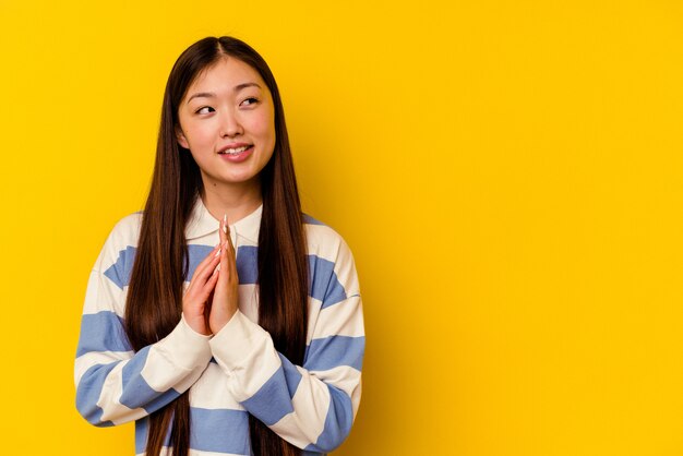 Jovem chinesa isolada em fundo amarelo, fazendo o plano em mente, estabelecendo uma ideia.