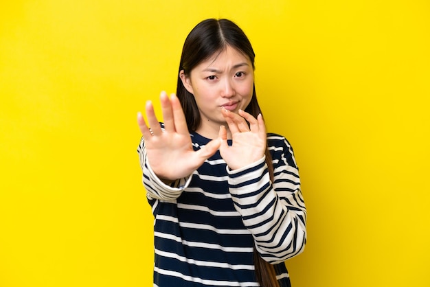 Jovem chinesa isolada em fundo amarelo nervoso esticando as mãos para a frente