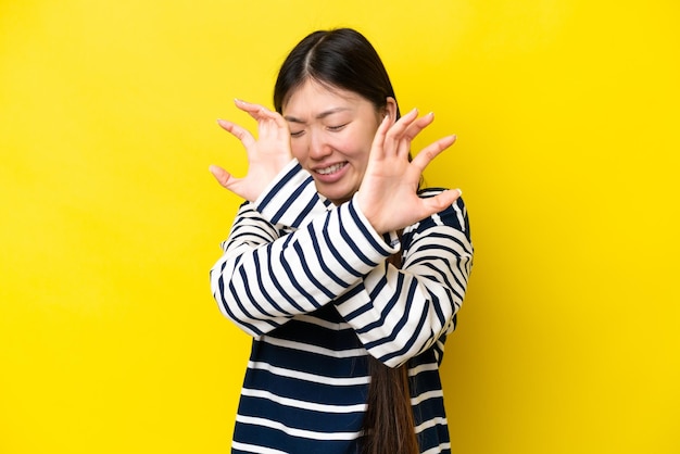 Jovem chinesa isolada em fundo amarelo nervoso esticando as mãos para a frente